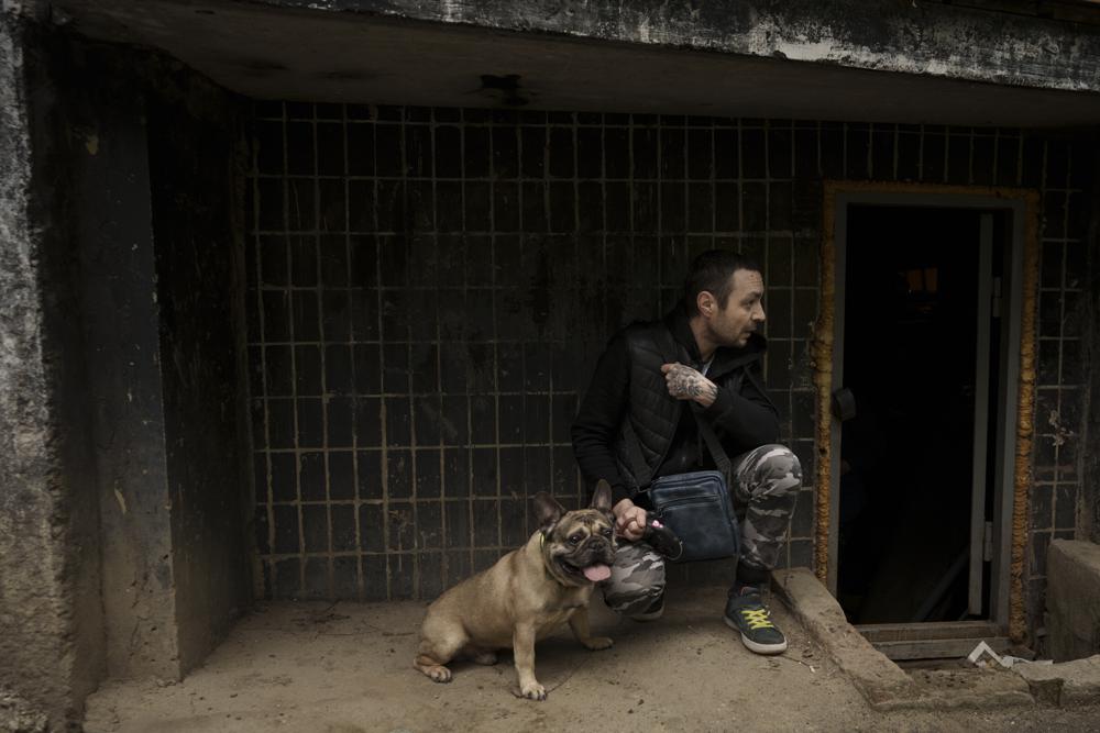 A man takes cover with his dog under a building as the sound of rockets is heard following a Russian bombardment in Kharkiv, Ukraine, Friday, April 22, 2022. (AP Photo/Felipe Dana)