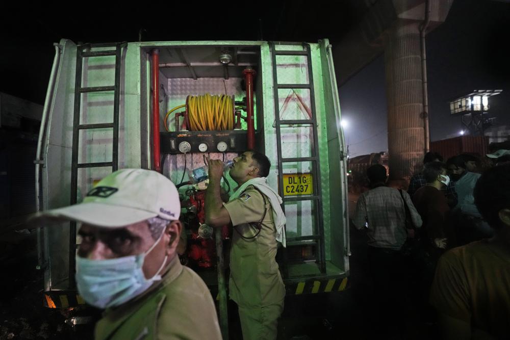 A fire official quenches his thirst after dousing a fire in a four storied building, in New Delhi, India, Saturday, May 14, 2022. A massive fire erupted in a four-storied building in the Indian capital on Friday, killing at least 19 people and leaving several injured, the fire control room said. Dozens of people have been rescued from the commercial building, mainly shops, in the Mundka area in the western part of New Delhi. (AP Photo/Manish Swarup)