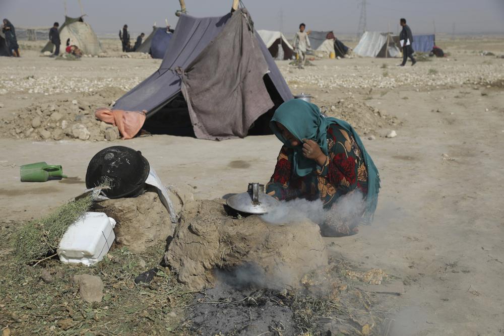 An internally displaced Afghan woman who fled her home due to fighting between the Taliban and Afghan security personnel, burns thorny twigs to make tea in a makeshift tent camp on a rocky patch of land on the edge of the city of Mazar-e-Sharif, northern Afghanistan, Thursday, July 8, 2021. Thousands of people have fled Taliban insurgents sweeping across northern Afghanistan, fearful of their harsh rule. (AP Photo/Rahmat Gul)