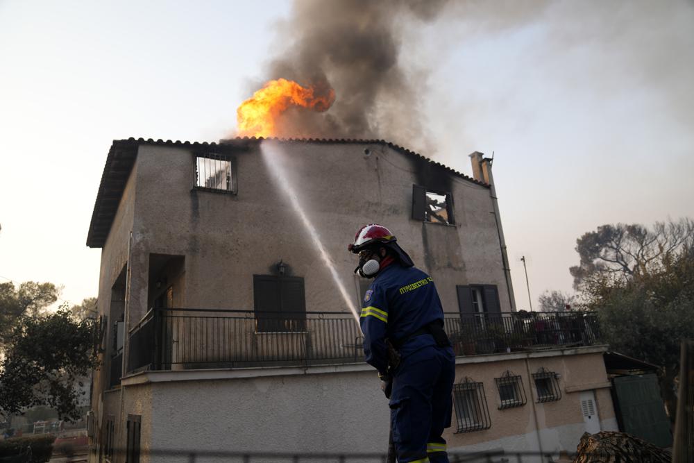 A firefighter tries to extinguish the flames at a burning house in Varibobi area, northern Athens, Greece, Wednesday, Aug. 4, 2021. More than 500 firefighters struggled through the night to contain a large forest blaze on the outskirts of Athens, which raced into residential areas Tuesday, forcing thousands to flee. It was the worst of 81 wildfires that broke out in Greece over the past 24 hours, amid one of the country's most intense heatwaves in decades. (AP Photo/Thanassis Stavrakis)