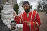 An Orthodox priest holds a commemorative ceremony to pay respect to the Chernobyl firefighters at a memorial in capital Kyiv, Ukraine, Tuesday, April 26, 2022. Firefighter sculptures at rear are covered with bags to protect against the Russian shelling. April 26 marks the 36th anniversary of the Chernobyl nuclear disaster. A reactor at the Chernobyl nuclear power plant exploded on April 26, 1986, leading to an explosion and the subsequent fire spewed a radioactive plume over much of northern Europe. (AP Photo/Efrem Lukatsky)