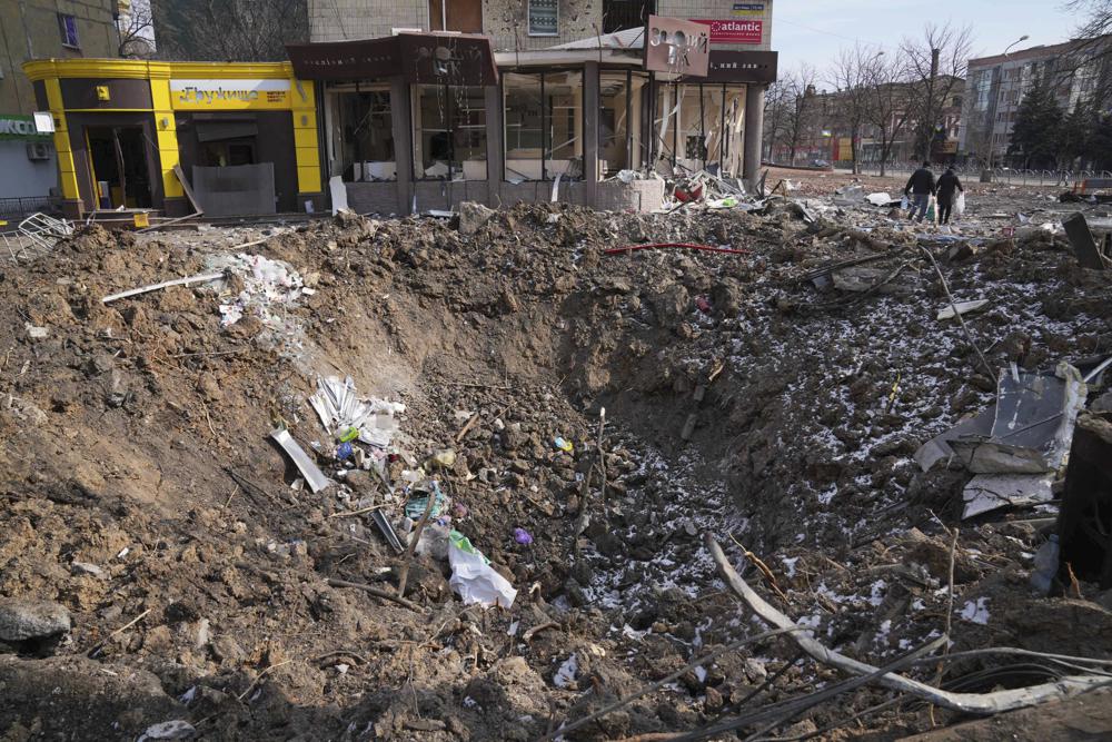 FILE - People walk past a crater from the explosion in Mira Avenue (Avenue of Peace) in Mariupol, Ukraine, March 13, 2022. Russia is bracing up for a massive new offensive in eastern Ukraine, hoping to reverse its fortunes on the battlefield after a catastrophic start of the invasion. (AP Photo/Evgeniy Maloletka, File)