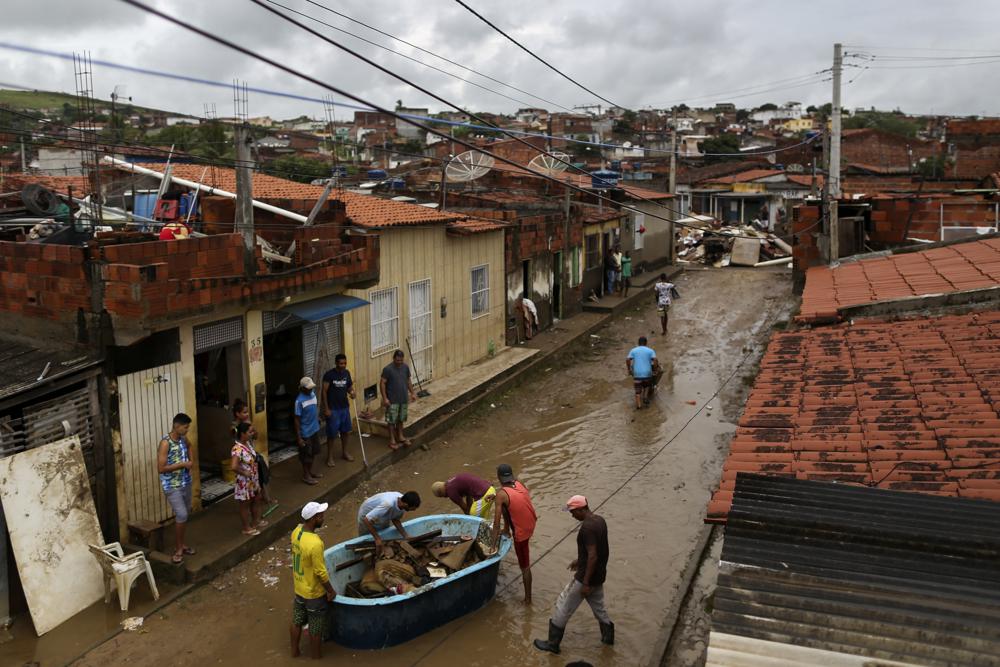 Residents clean out their flooded homes in Itapetinga, Bahia state, Brazil, Tuesday, Dec. 28, 2021. Two dams broke Sunday in northeastern Brazil, threatening worse flooding in a rain-drenched region that has already seen thousands of forced to flee their homes. (AP Photo/Raphael Muller)