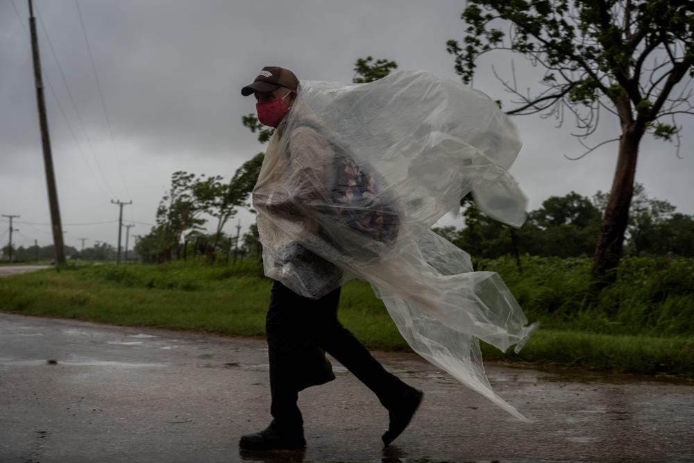 Un hombre se cubre con un plástico de la lluvia causada por el huracán Ida mientras de dirige a pie a Batabanó, en la provincia de Mayabeque, en Cuba, el viernes 27 de agosto de 2021. (AP Foto/Ramon Espinosa)