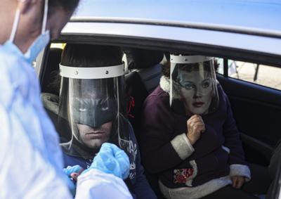 Un trabajador de la salud realiza una prueba rápida de COVID-19 a Ignacio Poblete, con un protector facial con la imagen de Batman, acompañado de su madre Marisol Aro, usando un protector facial con la imagen de la Mujer Maravilla, en Santiago, Chile, el sábado. 27 de junio de 2020. (AP Photo/Esteban Felix)