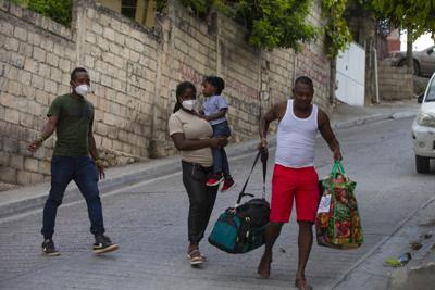 Jean Charles Celestin (derecha) carga con las pertenencias de su primo Jhon Celestin (izquierda), su esposa Delta De Leon y su hija Chloe, en Puerto Príncipe, Haití, el 22 de septiembre de 2021. Jhon Celestin llegó a la capital de Haití a bordo del último vuelo del día, Se había marchado tres años antes para buscar un empleo mejor pagado con el que mantener a su familia. (AP Foto/Joseph Odelyn)