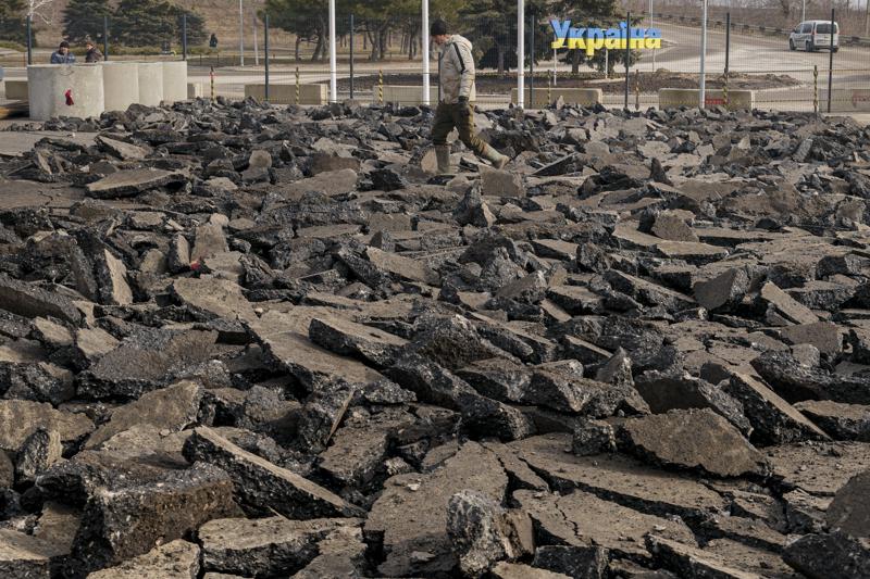 A construction worker is backdropped by the yellow-blue colored "Ukraine" road sign as the walks over broken pavement in a repairs area outside the crossing point from Ukrainian government to pro-Russian separatists controlled territory in Stanytsia Luhanska, the only crossing point which is open daily, in the Luhansk region, eastern Ukraine, Friday, Feb. 11, 2022. The chill of a Cold War hung over Eastern Europe again Friday, with Russian maneuvers and drills close to Ukraine, and NATO's chief boosting troop morale on the Black Sea. (AP Photo/Vadim Ghirda)