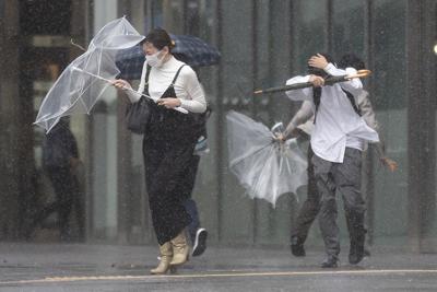 Varias personas intentan hacer frente a los fuertes aguaceros y vientos al paso del tifón Mindulle por la costa de Japón, el 1 de octubre de 2021, en Tokio. (AP Foto/Kiichiro Sato)