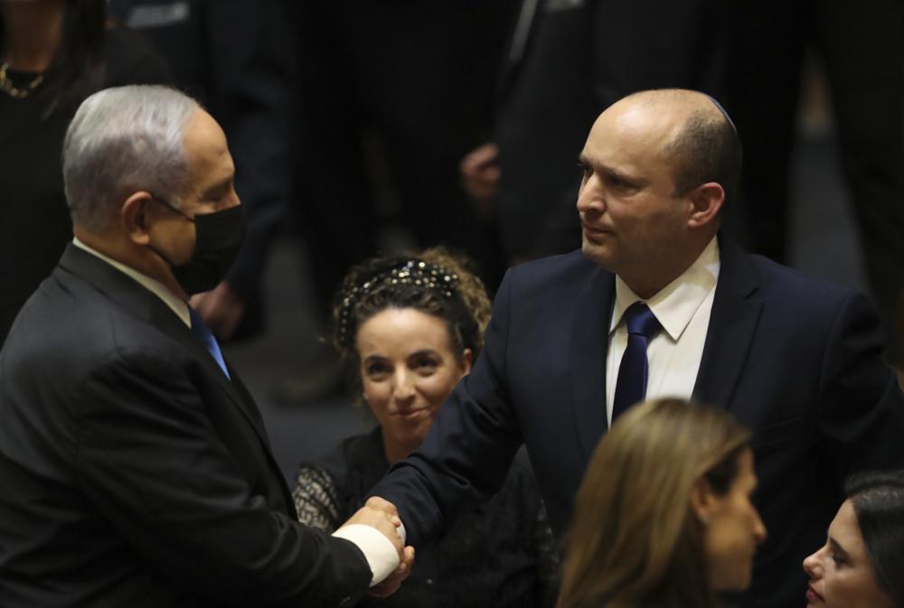 Israel's new prime minister Naftali Bennett shakes hands with outgoing prime minister Benjamin Netanyahu during a Knesset session in Jerusalem Sunday, June 13, 2021. Israel's parliament has voted in favor of a new coalition government, formally ending Netanyahu's historic 12-year rule. Naftali Bennett, a former ally of Netanyahu became the new prime minister (AP Photo/Ariel Schalit)