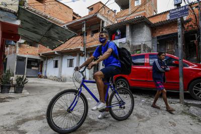 Jonathan Arcanjo, repartidor de la empresa Favela Brasil Xpress, circula en bicicleta por los callejones de la favela Paraisópolis de Sao Paulo, Brasil, para entregar un paquete el martes 31 de agosto de 2021, en medio de la pandemia de COVID-19. (AP Foto/Marcelo Chello)