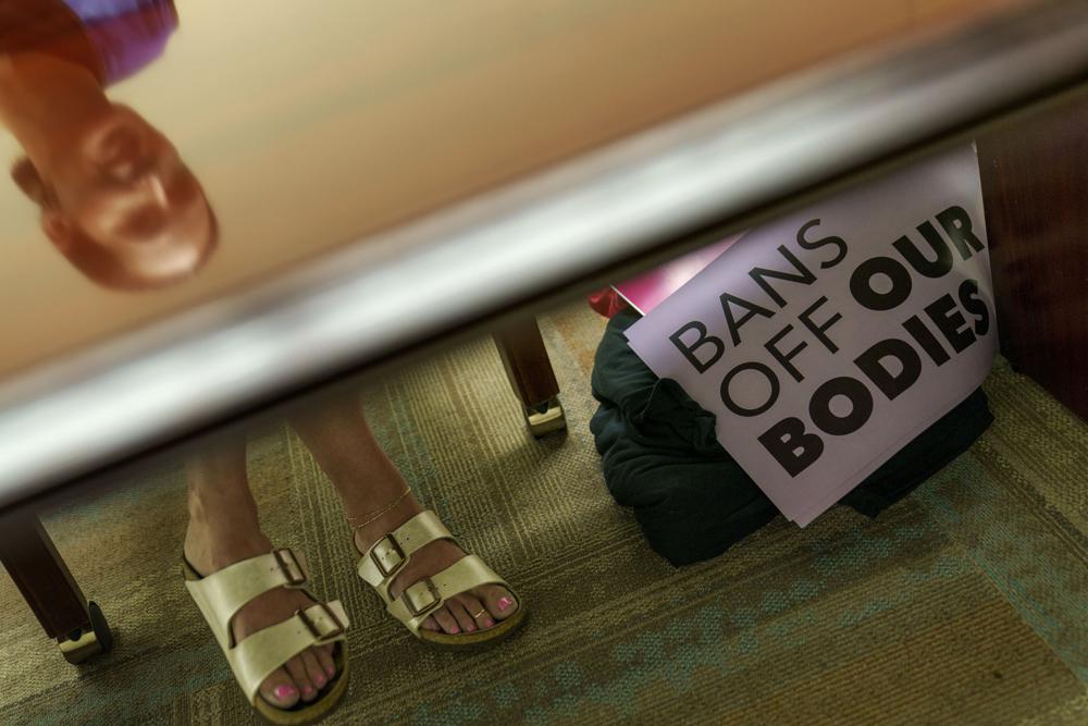 File - Planned Parenthood advocacy programs manager, Allison Terracio, is reflected in a table as signs sit in the clinic's office in Columbia, S.C., Friday, May 27, 2022. One year ago, the U.S. Supreme Court rescinded a five-decade-old right to abortion, prompting a seismic shift in debates about politics, values, freedom and fairness. (AP Photo/David Goldman, File)