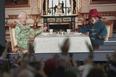 Una multitud observa un video en el que se ve a la reina Isabel II tomando el té con el oso Paddington en una pantalla grande durante el concierto del Jubileo de Platino ante el Palacio de Bukingham, Londres, el sábado 4 de junio de 2022, en el tercero de cuatro días de celebraciones para conmemorar los 70 años de servicio de la reina. (Victoria Jones/PA via AP)