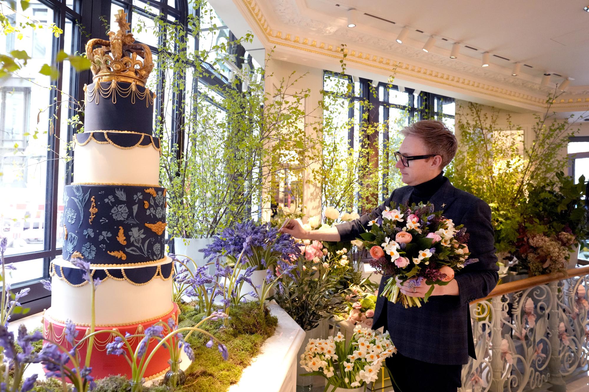 Philip Hamond, designer florist at the Dorchester Hotel, works alongside a display showing a Coronation themed cake and floral arrangements at the Dorchester Hotel in London, Thursday, April 20, 2023. The Dorchester Hotel, long a favorite with royals and celebrities, concocted a lavish, five-tier coronation cake and put up theater-style draping across its facade to re-create the decorations that it used to mark Queen Elizabeth II’s coronation in 1953 in preparation for King Charles III's coronation on May 6. (AP Photo/Kirsty Wigglesworth)