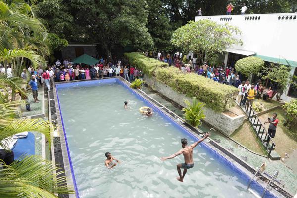 Protesters swim as onlookers wait at a swimming pool in president's official residence a day after it was stormed in Colombo, Sri Lanka, Sunday, July 10, 2022. Sri Lanka’s opposition political parties will meet Sunday to agree on a new government a day after the country’s president and prime minister offered to resign in the country’s most chaotic day in months of political turmoil, with protesters storming both officials’ homes and setting fire to one of the buildings in a rage over the nation’s economic crisis. (AP Photo/Eranga Jayawardena)