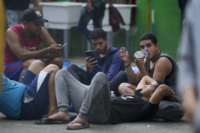 Migrantes venezolanos revisan sus teléfonos móviles mientras esperan en un albergue temporal en Ciudad de Panamá, el martes 25 de octubre de 2022. (Foto AP/Arnulfo Franco)