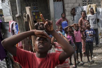 Un niño señala hacia un helicóptero que trae ayuda para los sobrevivientes del terremoto en un vecindario cerca del aeropuerto, el jueves 19 de agosto de 2021, en Les Cayes, Haití. (AP Foto/Matías Delacroix)