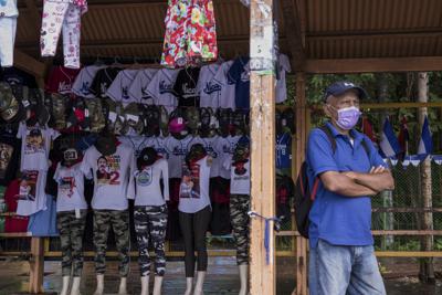 Un hombre espera un autobús de transporte público junto a un puesto que vende camisetas, banderas y sombreros, con un tema sandinista, en una parada de autobús en Managua, Nicaragua, el miércoles 3 de noviembre de 2021. Nicaragua está preparada para celebrar elecciones el 7 de noviembre en las que el presidente Daniel Ortega busca un cuarto mandato consecutivo, pero esas elecciones se han vuelto casi irrelevantes por el encarcelamiento por parte del gobierno de críticos y siete posibles retadores.  (AP Foto / Andres Nuñez)