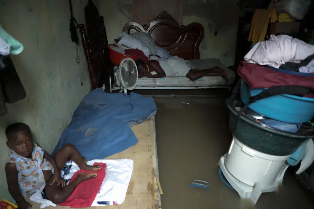 A mother and her son rest in their flooded house after a heavy rain, in Port-au-Prince, Haiti, Saturday, June 3, 2023. (AP Photo/Odelyn Joseph)