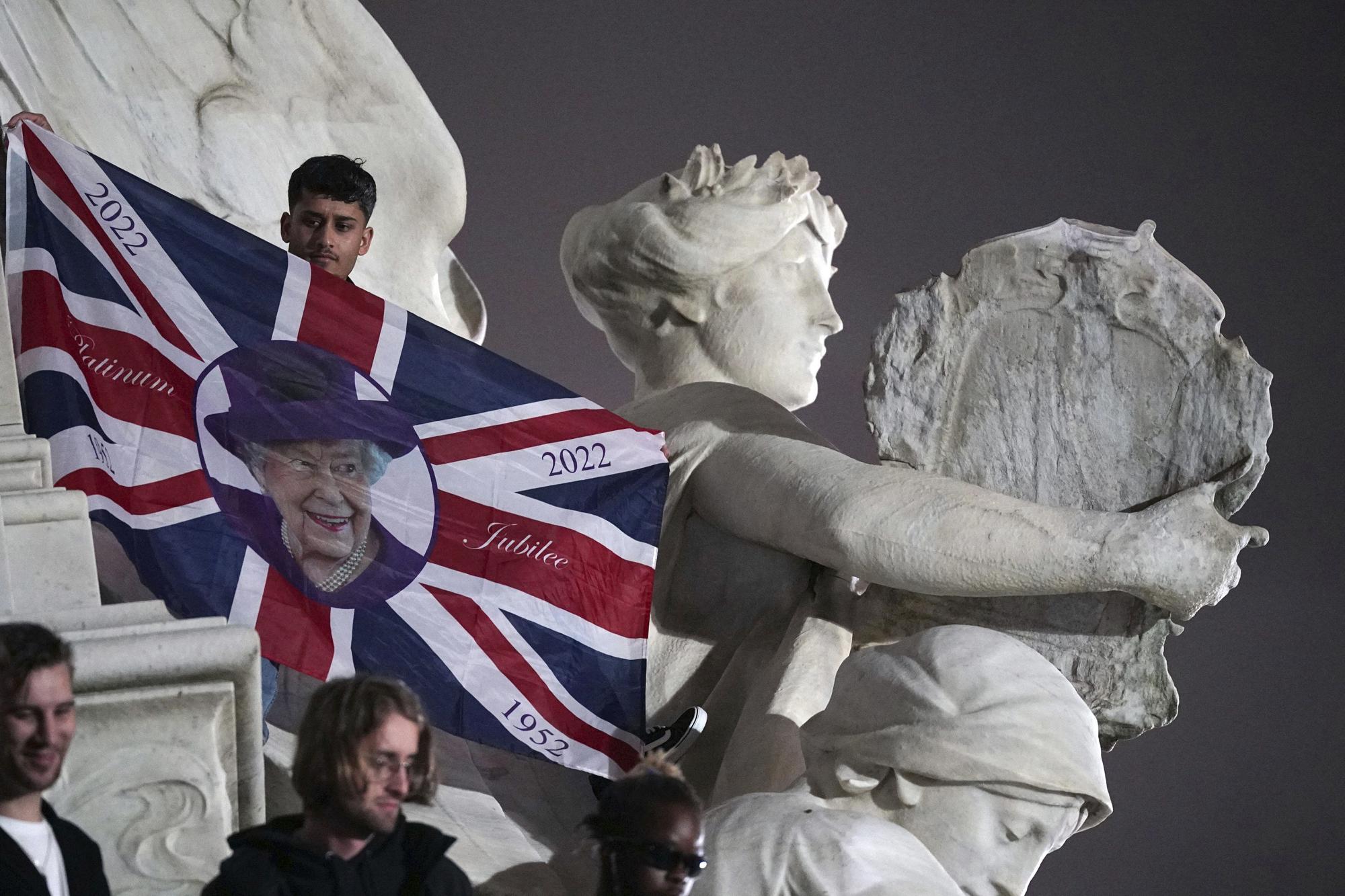 Mourners on Queen Victoria Memorial outside Buckingham Palace in central London, following the announcement of the death of Queen Elizabeth II, Thursday, Sept. 8, 2022. Britain's longest-reigning monarch and a rock of stability across much of a turbulent century, has died. She was 96. (Yui Mok/PA via AP)