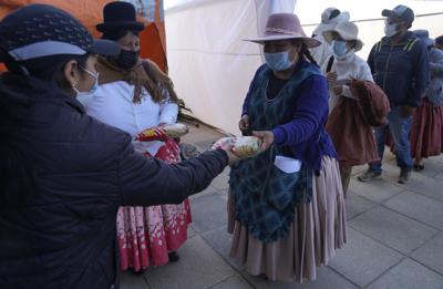 Una trabajadora municipal le entrega una bolsa de fideos a una mujer después de que la inocularon con una dosis de la vacuna Sinopharm contra el COVID-19 durante una campaña de inmunización para mayores de 18 años, en El Alto, Bolivia, el sábado 14 de agosto de 2021. Autoridades municipales de El Alto ofrecen fideos y arroz a los vecinos que accedan a vacunarse contra el nuevo coronavirus. (Foto AP/Juan Karita)