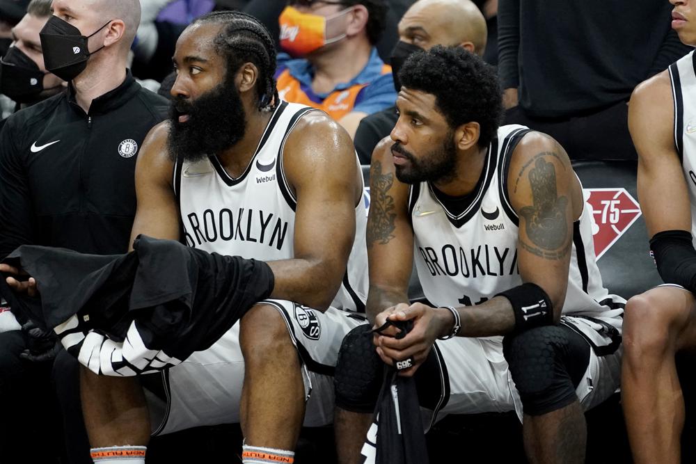 Brooklyn Nets guard James Harden, left, and guard Kyrie Irving watch from the bench during the second half of an NBA basketball game against the Phoenix Suns, Tuesday, Feb. 1, 2022, in Phoenix. The Suns defeated the Nets 121-111. (AP Photo/Matt York)