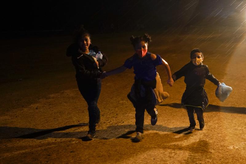 FILE - In this May 11, 2021 file photo three young migrants hold hands as they run in the rain at an intake area after turning themselves in upon crossing the U.S.-Mexico border in Roma, Texas. An official says the Biden administration has begun flying some Central American families deep into Mexico as authorities encounter more families and unaccompanied children at the U.S.-Mexico border. (AP Photo/Gregory Bull, File)