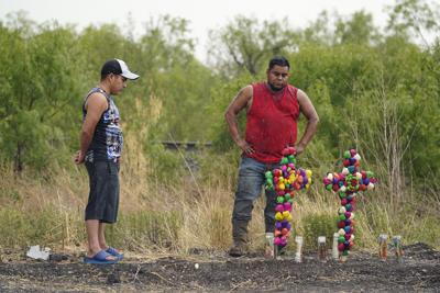 La lluvia cae sobre dos hombres que observan dos cruces en el sitio donde las autoridades hallaron a docenas de personas muertas dentro de un tractocamión, el martes 28 de junio de 2022, en San Antonio. (AP Foto/Eric Gay)