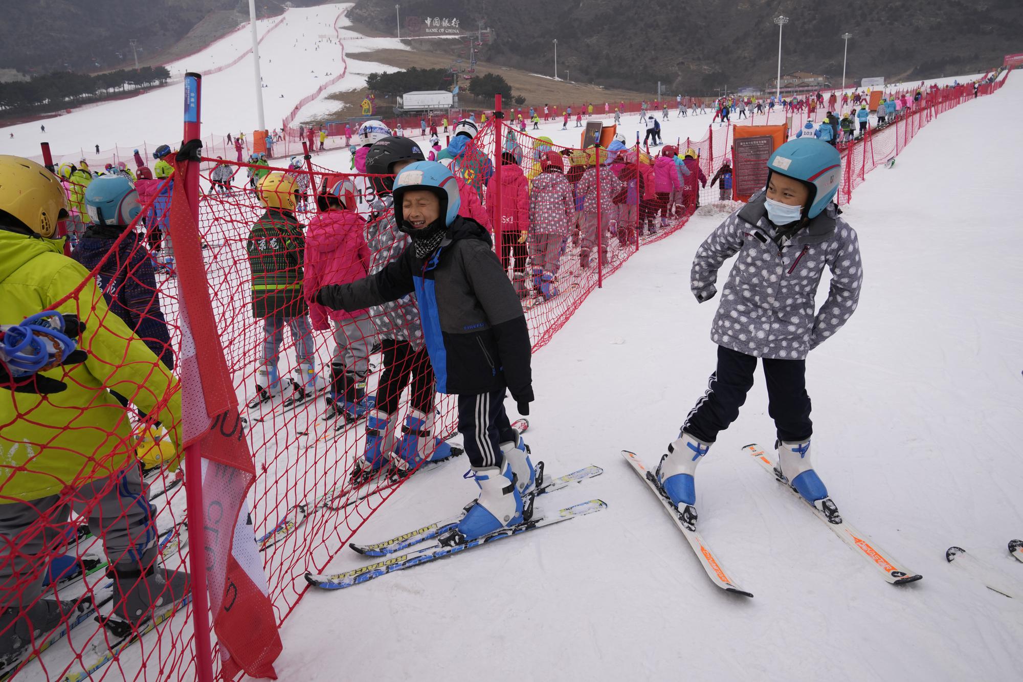 School children play near a long line up to the bunny slope at the Vanke Shijinglong Ski Resort in Yanqing on the outskirts of Beijing, China, Thursday, Dec. 23, 2021. The Beijing Winter Olympics is tapping into and encouraging growing interest among Chinese in skiing, skating, hockey and other previously unfamiliar winter sports. It's also creating new business opportunities. (AP Photo/Ng Han Guan)