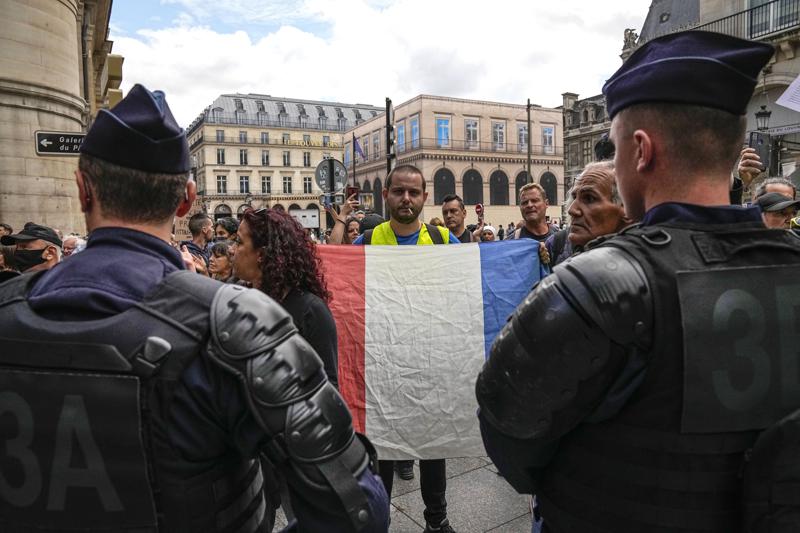 An anti heath pass demonstrator holds a French flag as he faces police officers outside the Constitutional Council in Paris, Thursday, Aug. 5,2021. France's Constitutional Council is deciding on Thursday whether the health pass that is to open the doors and terraces to cafes, restaurants, trains and hospitals starting next week is in line with the nation's most cherished principles. (AP Photo/Michel Euler)