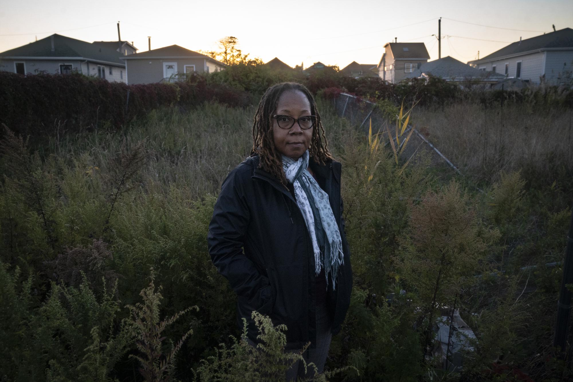 Sonia Moise, a resident of the Edgemere neighborhood, stands by an overgrown empty lot on a residential street damaged by Superstorm Sandy, Thursday, Oct. 20, 2022, in the Queens borough of New York. "They tell me that we're one peninsula — no we're not. It's a tale of two peninsulas," said Edgemere resident Moise, whose home filled with seawater during Sandy, her car carried off by the tide. (AP Photo/John Minchillo)