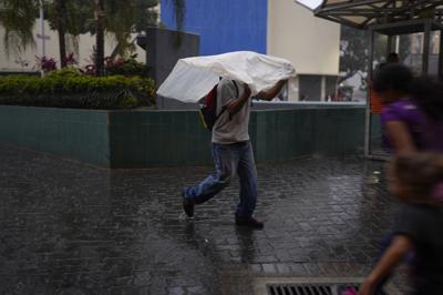 Un hombre usa una bolsa de plástico para protegerse de la lluvia en Caracas, el miércoles 29 de junio de 2022. (AP Foto/Ariana Cubillos)