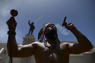 Gypsy Cordova echa humo y agita una maraca frente a la estatua del explorador español Juan Ponce de León durante una protesta para exigir que se retiren las estatuas y los nombres de las calles que recuerdan a la opresión colonial, en San Juan, Puerto Rico, el 11 de julio de 2020. Desconocidos derribaron la estatua antes de una visita de Felipe VI a Puerto Rico, el 24 de enero de 2022. (Foto AP/Carlos Giusti, Archivo)