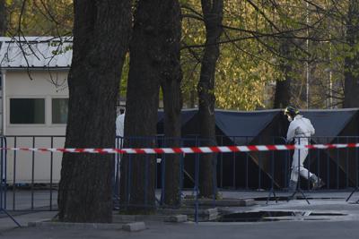 Un agente, con un equipo de protección, cubre el lugar donde un auto impactó contra la cerca de acceso a la embajada de Rusia, en Bucarest, Rumanía, el 6 de abril de 2022. (AP Foto/Andreea Alexandru)