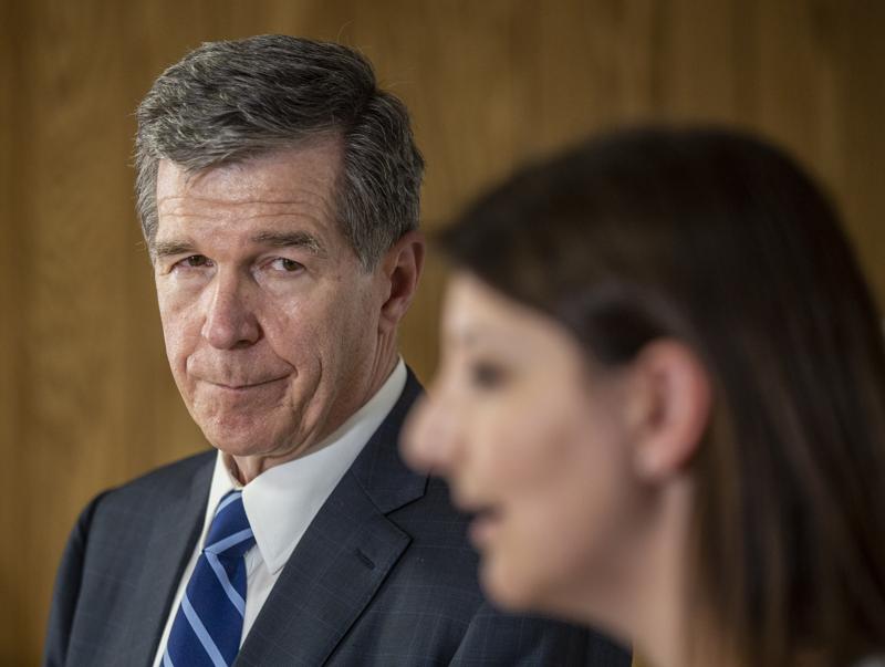 North Carolina Governor Roy Cooper looks on as Dr. Mandy Cohen speaks to the media after their tour of a COVID-19 vaccine clinic at the Pine Hall Brick plant in Madison, N.C., on Thursday, May 27, 2021. (Woody Marshall/News & Record via AP)