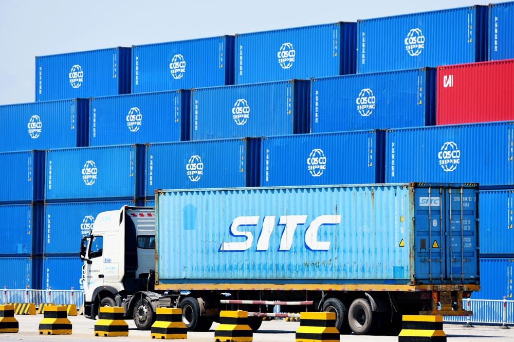 A container truck passes by stacks of COSCO containers on a dockyard of a port in Qingdao in eastern China's Shandong province Friday, June 4, 2021. China's exports surged nearly 28% in May while imports jumped 51% as demand rebounded in the U.S. and other markets where the pandemic is waning, though growth is leveling off after a stunning recovery from last year's slump. (Chinatopix via AP)