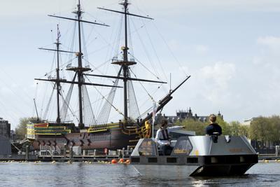 UN barco eléctrico pasa junto a una réplica a tamaño real del mercante de tres mástiles del siglo XVIII Amsterdam en el Museo Marítimo Nacional en Ámsterdam, el jueves 20 de mayo de 2021. (AP Foto/Peter Dejong)