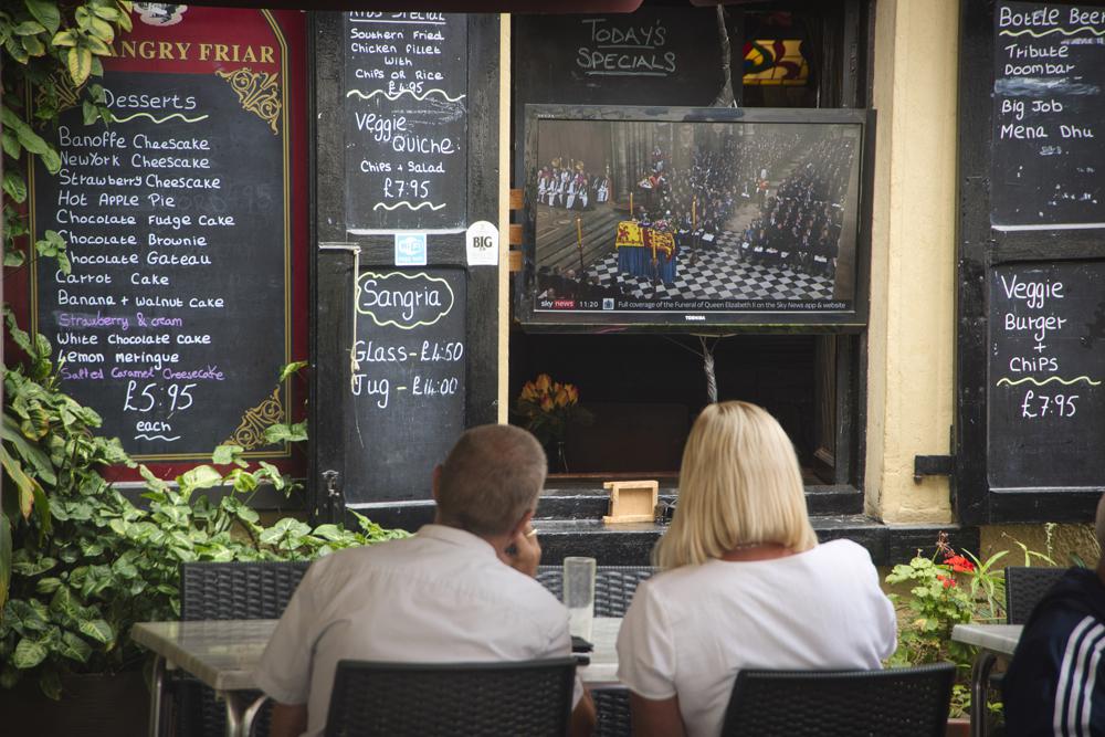 Two people watch on tv the funeral service of Queen Elizabeth II, in Gibraltar, Monday, Sept. 19, 2022. (AP Photo/Marcos Moreno)