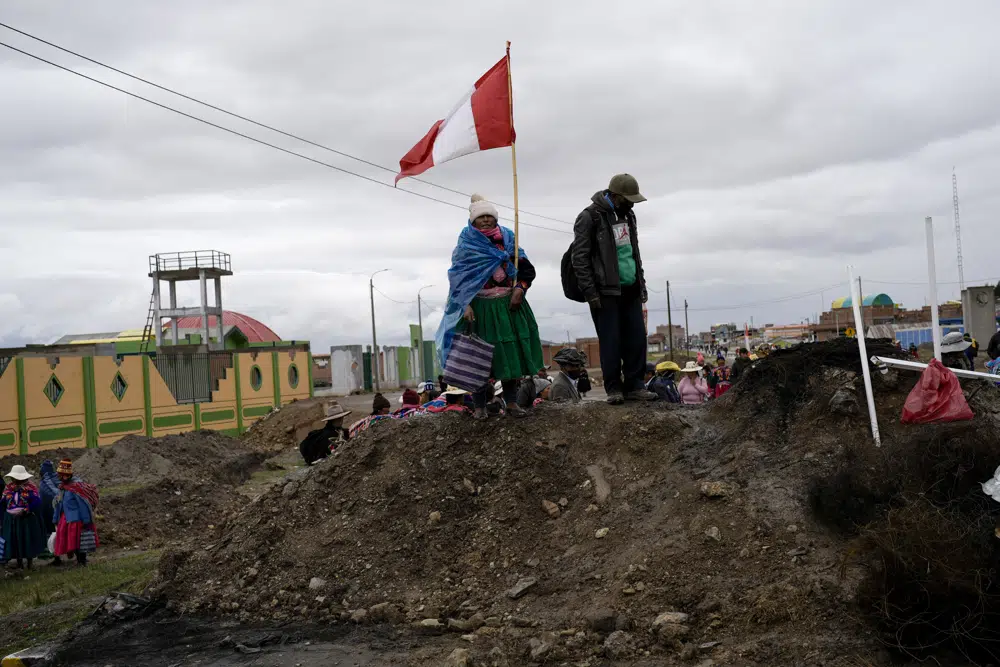 FILE - An Aymara woman, holding a Peruvian national, stands on a pile of dirt serving as a roadblock set up by anti-government protesters, in Acora, southern Peru, Jan. 29, 2023. Peruvians have been protesting since early December, when former President Pedro Castillo was impeached after a failed attempt to dissolve Congress. His vice president, Boluarte, immediately took over — and has faced strong opposition ever since. (AP Photo/Rodrigo Abd, File)