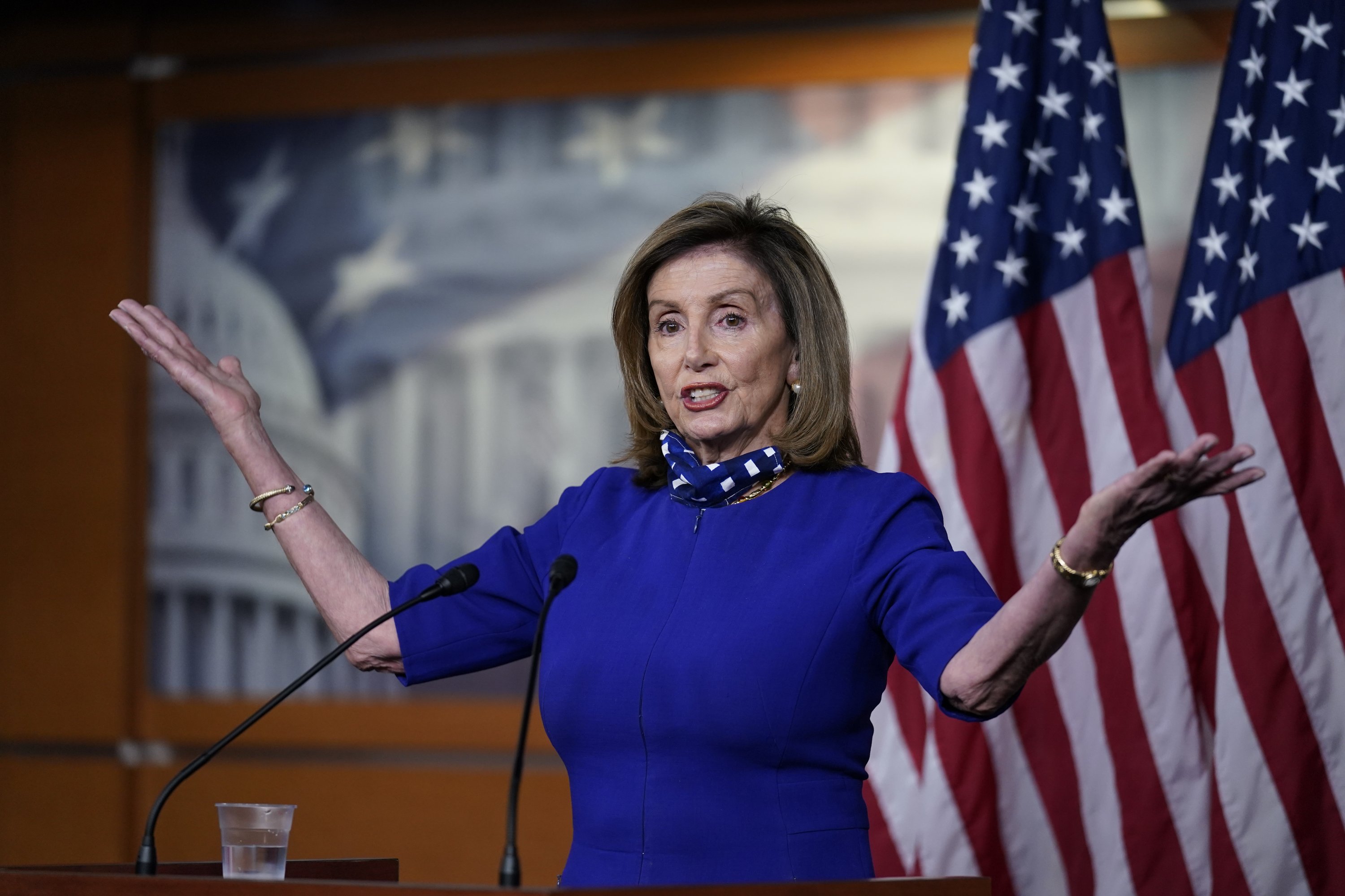 Speaker Nancy Pelosi in front of flags, at a podium