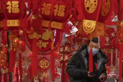 Un hombre, con mascarilla para protegerse del coronavirus, compra decoraciones para el Año Nuevo Lunar en un puesto en Beijing, el 7 de enero de 2023. (AP Foto/Andy Wong)