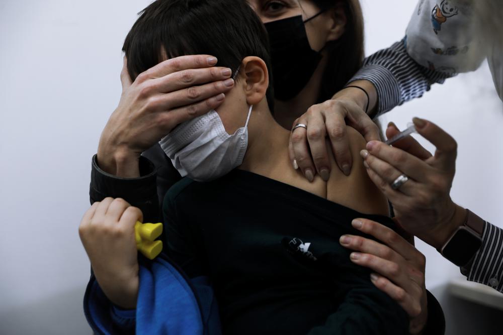 Israeli child Liam Lev Tov, 6, in the arms of his mother, receives a Pfizer-BioNTech COVID-19 vaccine from medical staff at Clalit Health services in Tel Aviv, Israel, Tuesday, Nov. 23, 2021. Israel begins coronavirus vaccination campaign for children aged 5 to 11. (AP Photo/Oded Balilty)