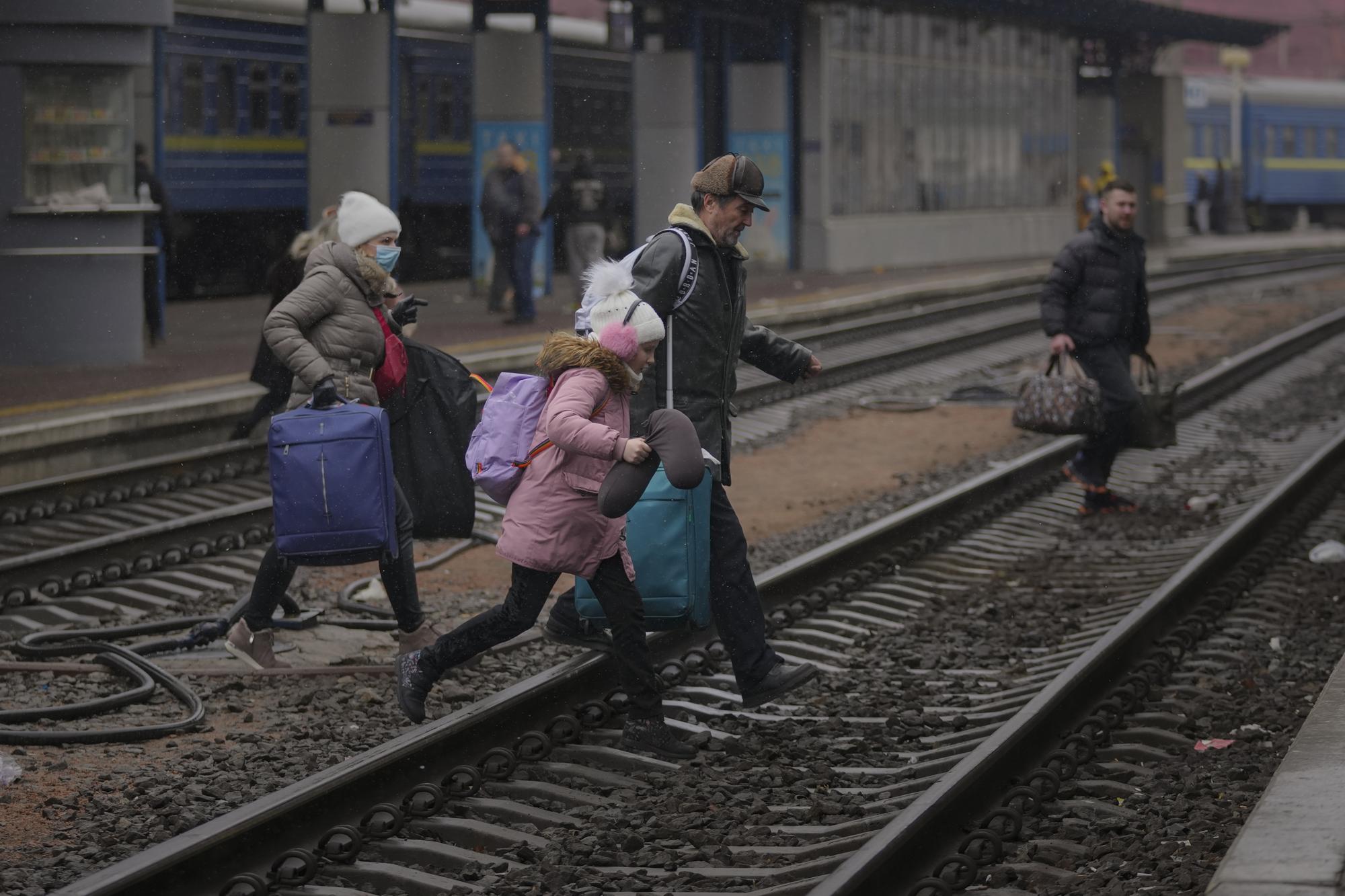 A family runs over the tracks trying to board a Lviv bound train, in Kyiv, Ukraine, Thursday, March 3, 2022. (AP Photo/Vadim Ghirda)