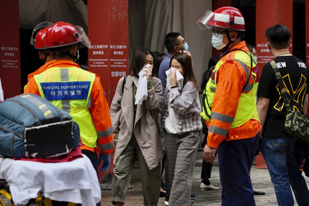 Gente a pie delante del World Trade Center, en el popular distrito comercial de Causeway Bay, Hong Kong, el miércoles 15 de diciembre de 2021. Docenas de personas estaban atrapadas el miércoles en la azotea de un rascacielos de Hong Kong en el que ardía un gran incendio, mientras los bomberos trataban de rescatarlas y apagar las llamas.  (AP Foto / Kin Cheung)