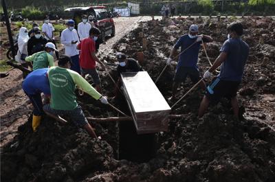 Unos trabajadores bajan un ataúd durante la inhumación de una víctima fatal de COVID-19, en una zona especial para esos cadáveres en el cementerio público de Jombang, el lunes 21 de junio de 2021 en Tangerang, en las afueras de Yakarta, Indonesia. (AP Foto/Tatan Syuflana)