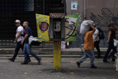 Peatones pasan junto a un teléfono inactivo de la compañía telefónica estatal venezolana CANTV en Caracas el 13 de mayo del 2022. En un alejamiento de su modelo socialista, el gobierno de Venezuela planea abrir a inversiones privadas varias compañías estatales en sectores vitales, parte de sus esfuerzos para responder a la necesidad de capital de capital para negocios con pocas inversiones.  (AP Foto/Ariana Cubillos)