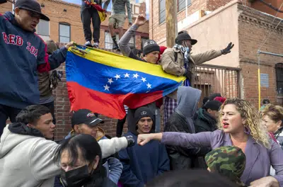 Un migrante de varios, a la izquierda, choca el puño con una residente local que los apoya en el centro de El Paso, Texas, el sábado 7 de enero de 2023. Al fondo varios migrantes muestran una bandera venezolana. (AP Foto/Andres Leighton)