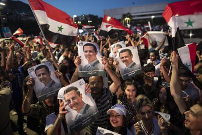 Simpatizantes del presidente Bashar Assad agitan banderas y sostienen retratos de él en la plaza Omayyad, en Damasco, Siria, después de que se anunciara que él gobernante ganó la reelección. (AP Fhoto/Hassan Ammar)