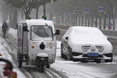 Un repartidor pasa junto a un auto cubierto de nieve recién caída en Beijing, China, el domingo 7 de noviembre de 2021. Una tormenta al principio de la temporada cubrió de nieve buena parte del norte de China, incluida la capital, Beijing, y provocó cortes de carreteras y cancelaciones de vuelos. (AP Foto/Ng Han Guan)