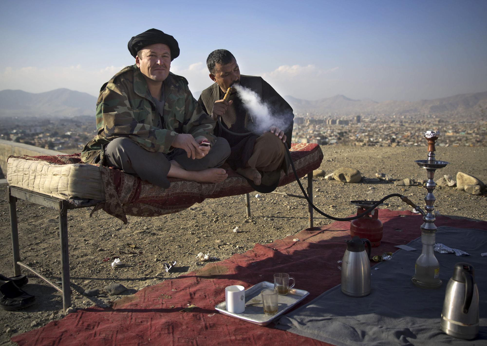 FILE - In this Nov. 25, 2013 file photo, police officers smoke a water pipe as they enjoy a quiet moment at their checkpoint overlooking Kabul, Afghanistan. (AP Photo/Anja Niedringhaus, File)