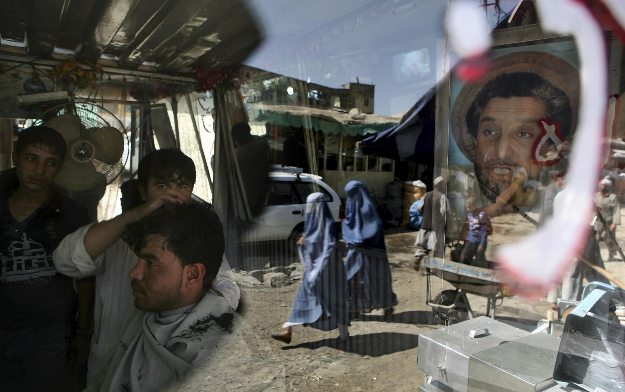 An Afghan barber works on a customer in his shop as a portrait of Afghanistan national hero Ahmad Shah Massoud adorns its door in Kabul, Afghanistan, Tuesday, Sept. 29, 2009. (AP Photo/Altaf Qadri)